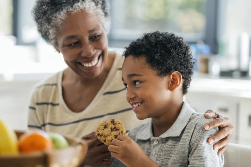 Grandmother and grandson sharing a chocolate chip cookie in a sunlit kitchen
