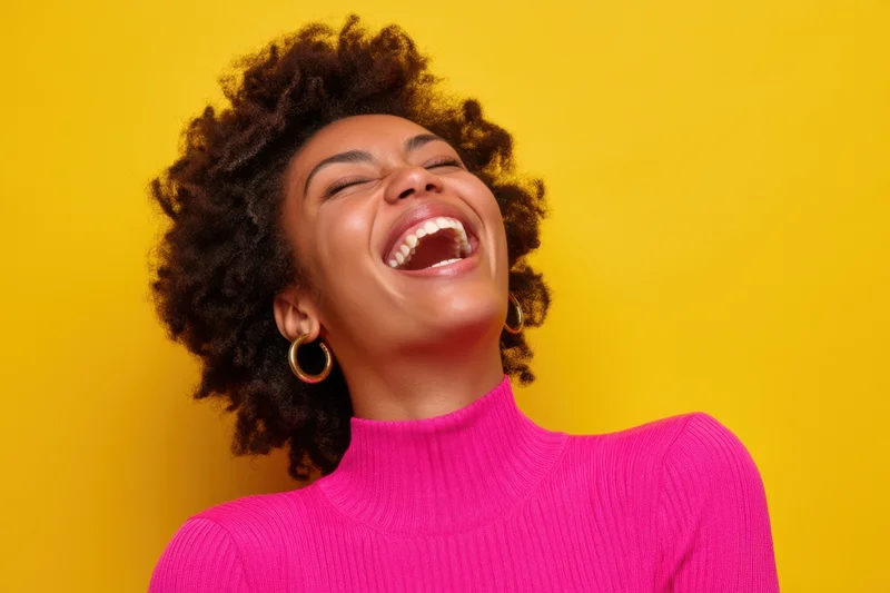 Young black woman laughing joyfully in bright pink ribbed turtleneck against yellow background