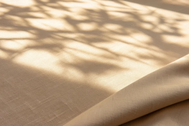 Beige fabric with dappled leaf shadows and soft folds, lit by natural sunlight