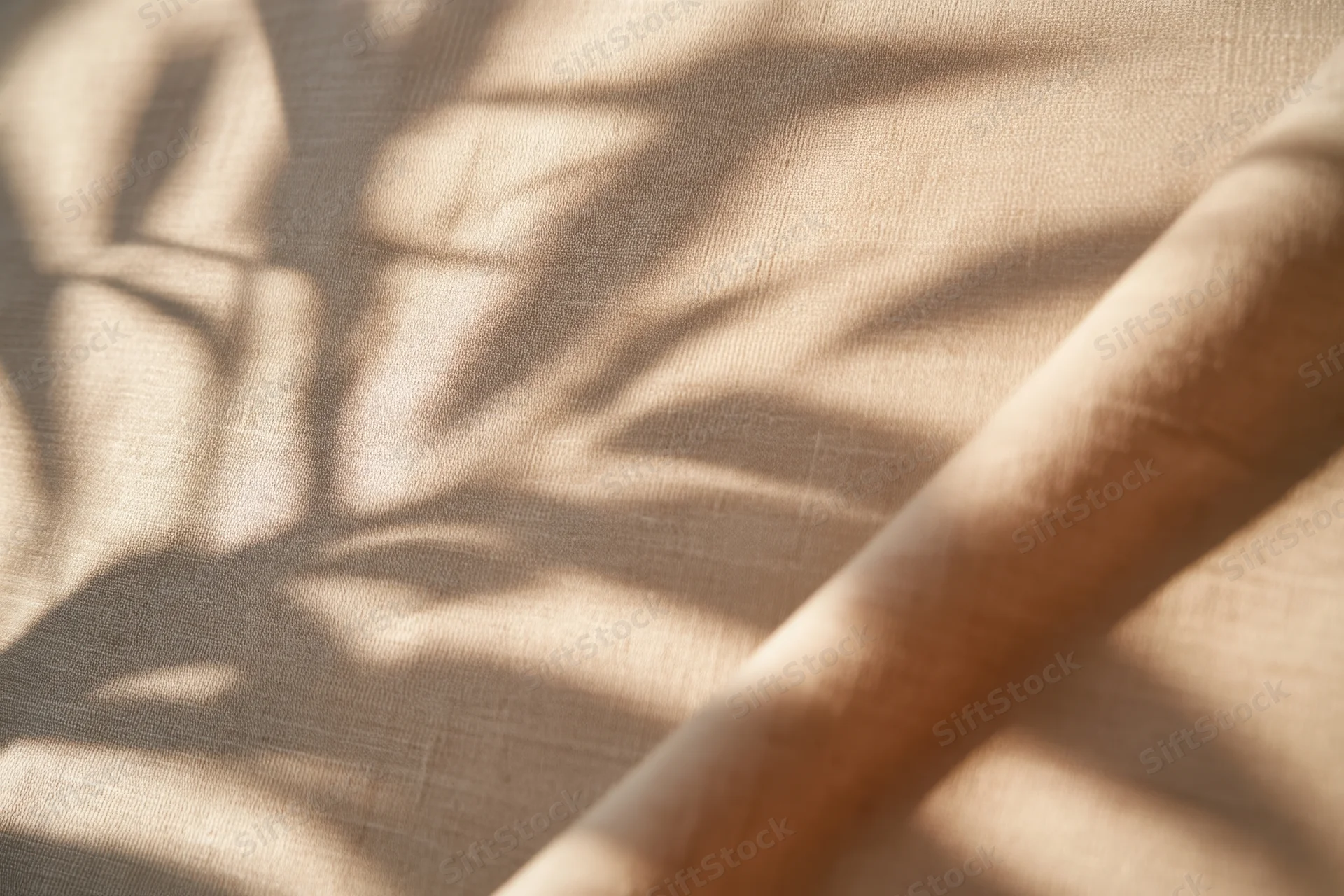 Dappled leaf shadows on a light beige fabric surface in soft sunlight