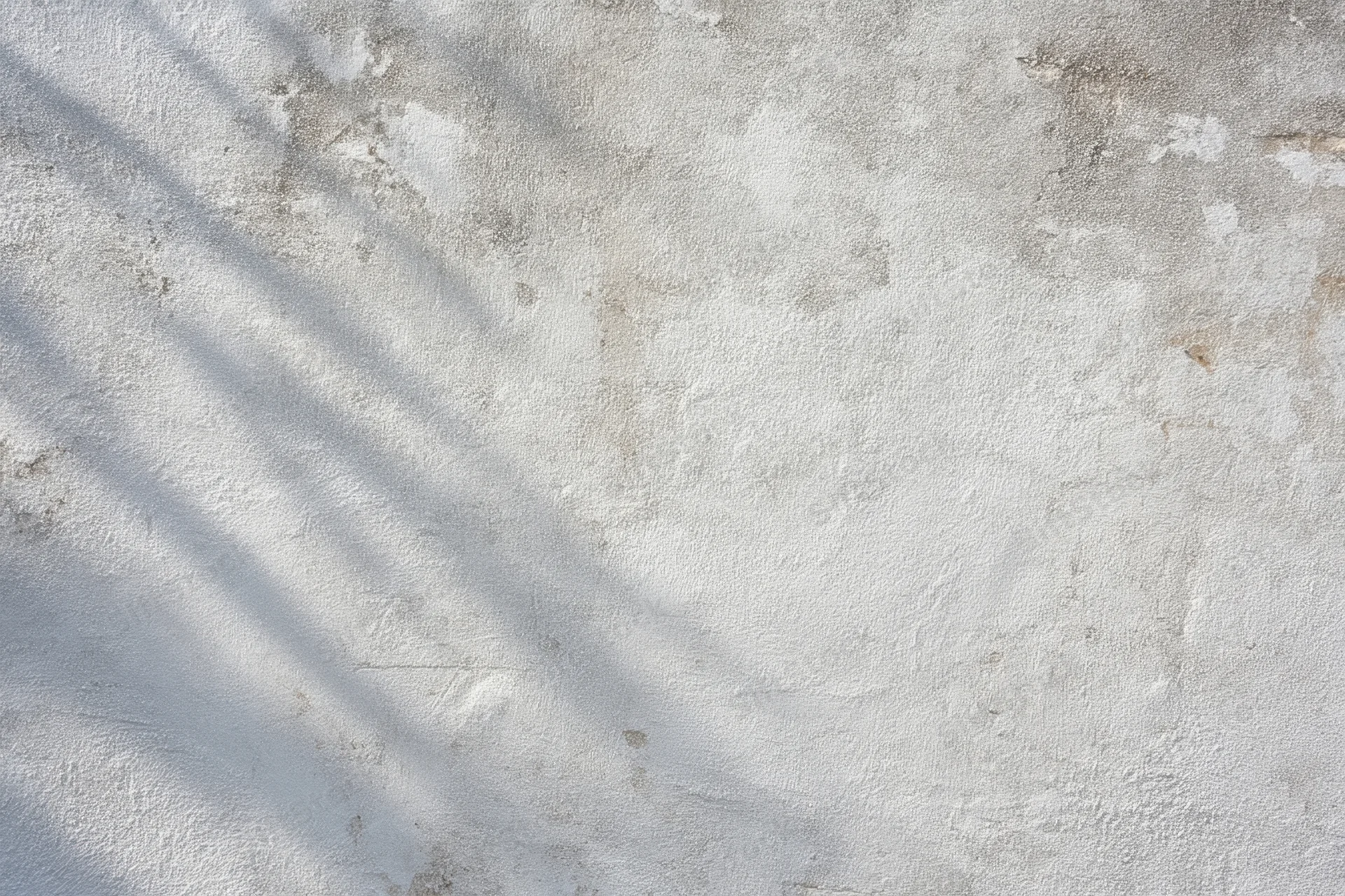 Weathered gray concrete wall with diagonal shadows and textured surface