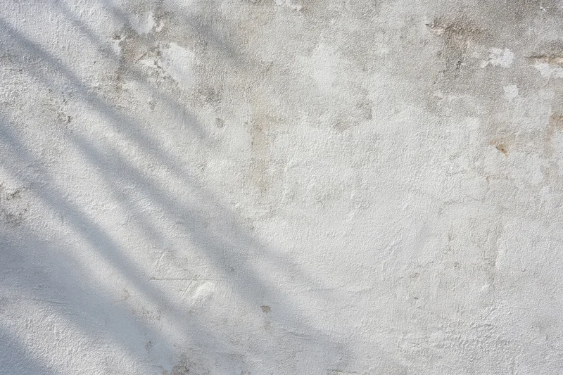 Weathered gray concrete wall with diagonal shadows and textured surface