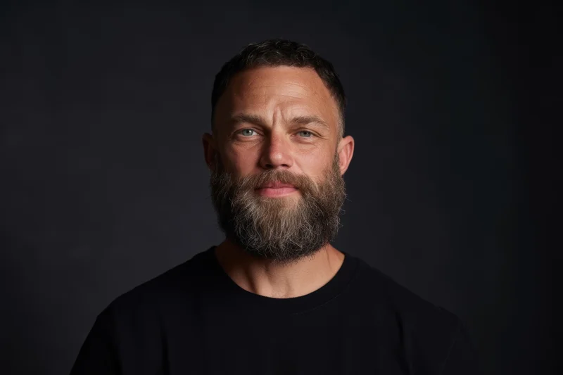 Man with full beard and short dark hair wearing black t-shirt in studio portrait