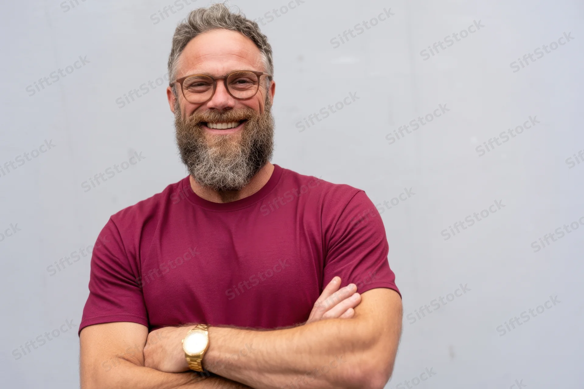 Middle-aged man with full beard and glasses smiling with arms crossed against light gray background