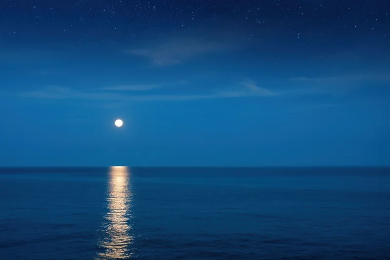 Full moon over calm ocean at night with starry sky and moonlight reflection on water surface