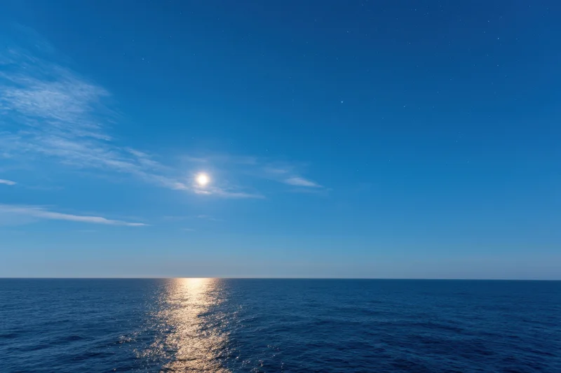Full moon glowing over calm ocean at night with reflection on water surface