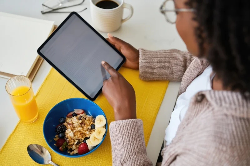 Woman reading on tablet at breakfast table with cereal and juice
