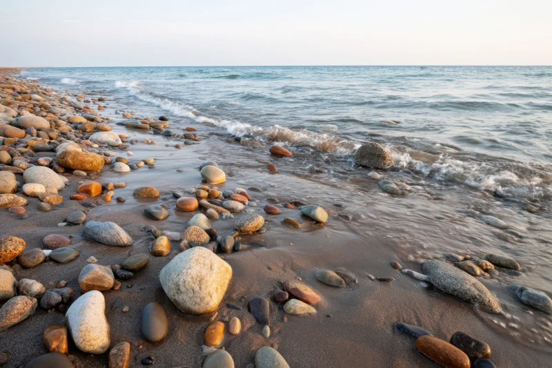 Smooth pebbles scattered across wet sand at the shoreline with gentle waves rolling in from the ocean
