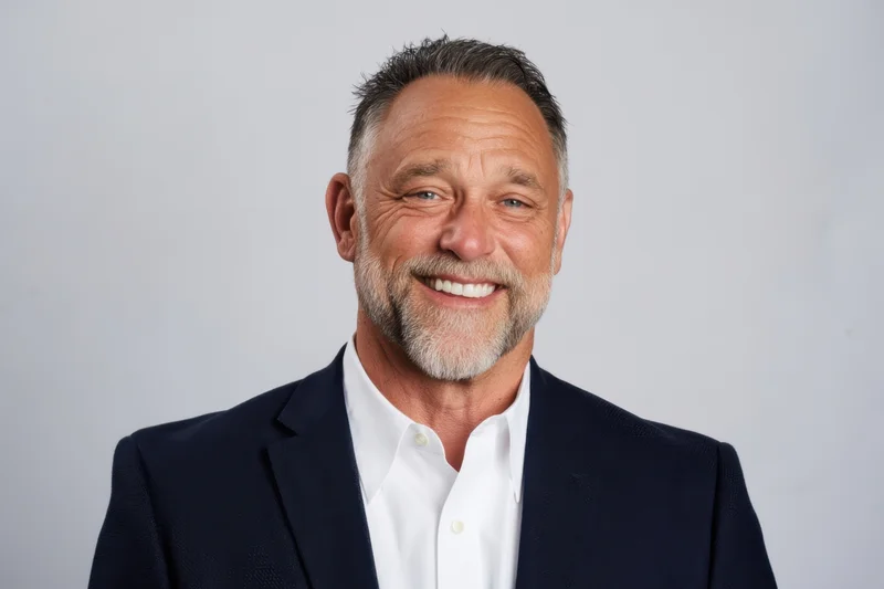 Smiling man in navy blazer and white shirt standing against plain background