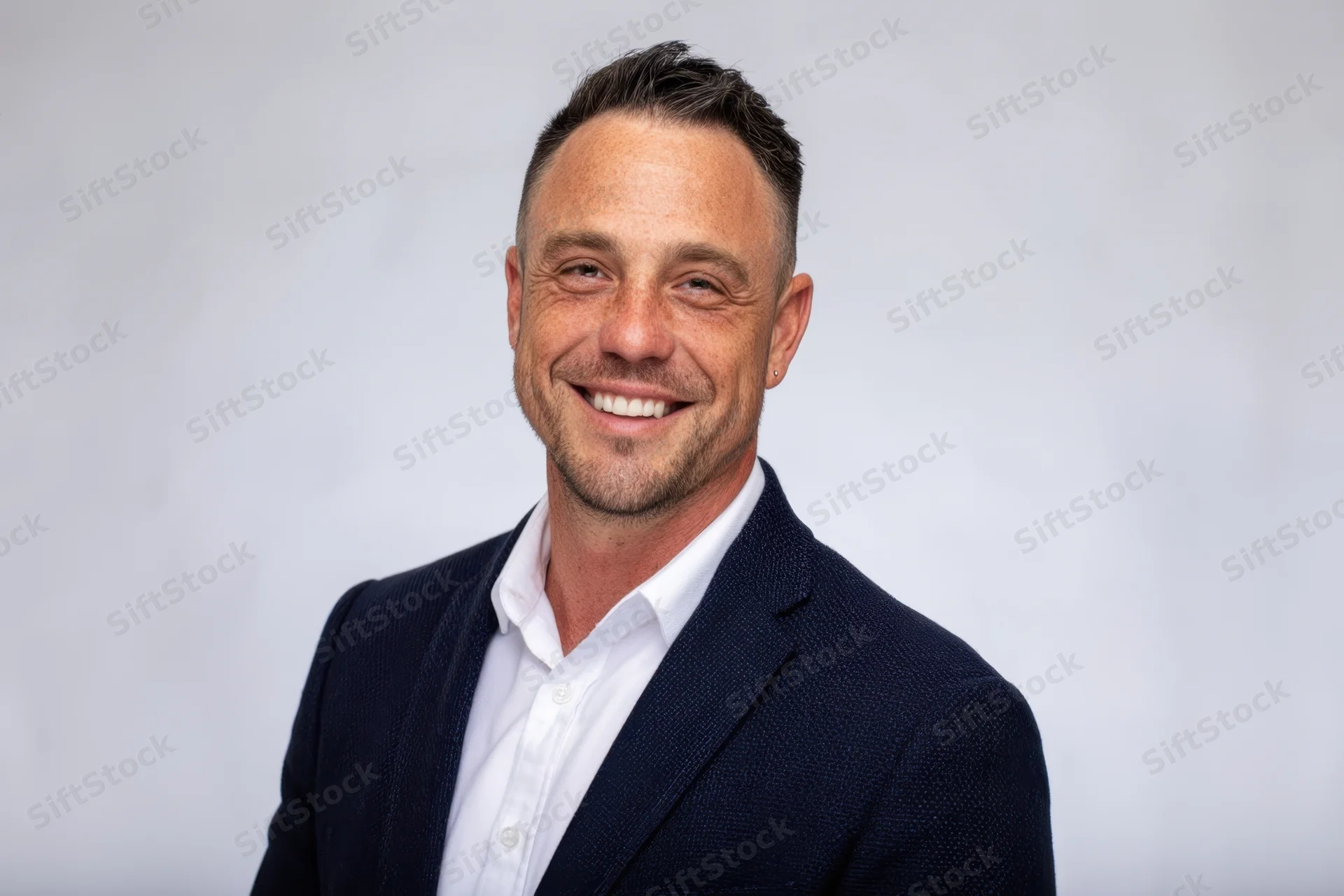 Smiling man in navy blazer and white shirt standing against plain background