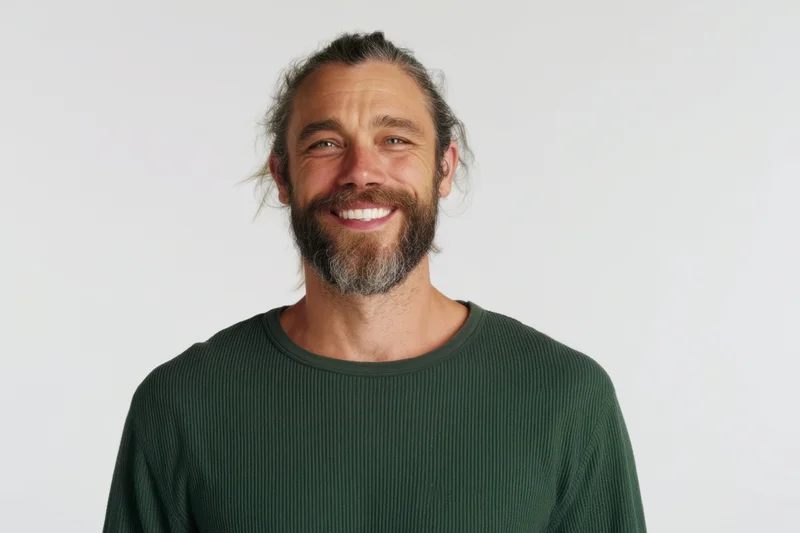 Smiling man with beard and tied-back hair in green ribbed sweater against white background
