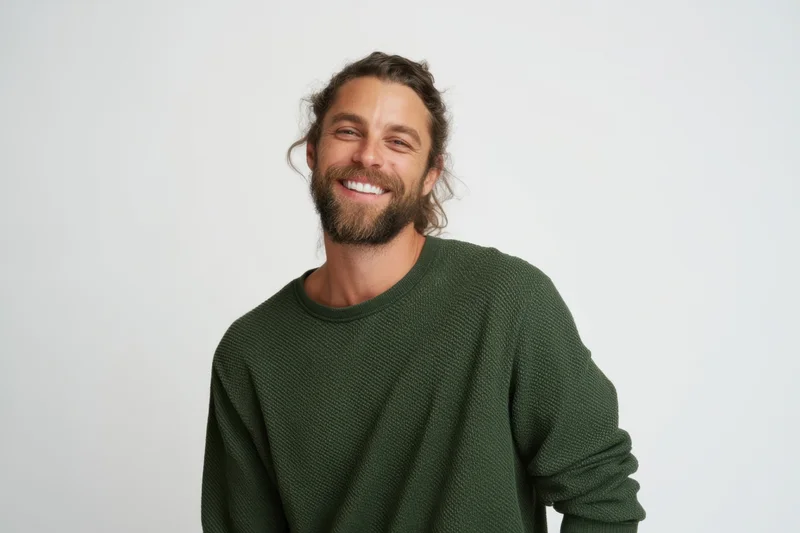Smiling man with beard and long hair tied back wearing green sweater in studio portrait