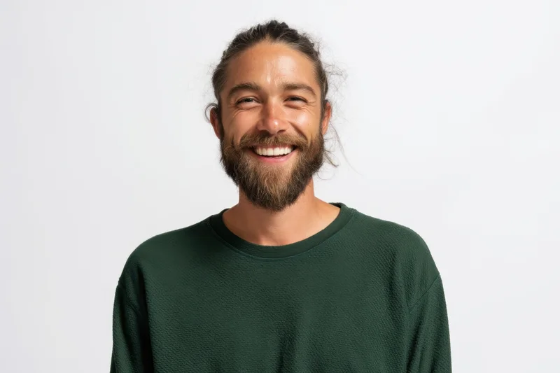 Smiling man with beard and hair tied back wearing green sweater in studio portrait