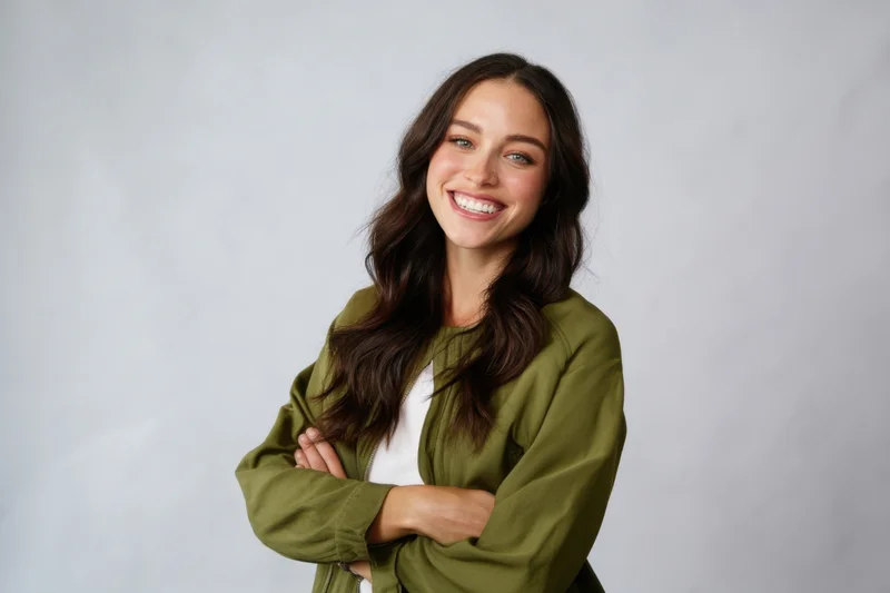 Smiling woman with arms crossed wearing olive green jacket over white tshirt in studio setting