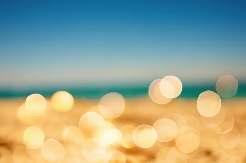 Sunlit beach with golden sand and blue sky, blurred foreground of bokeh lights