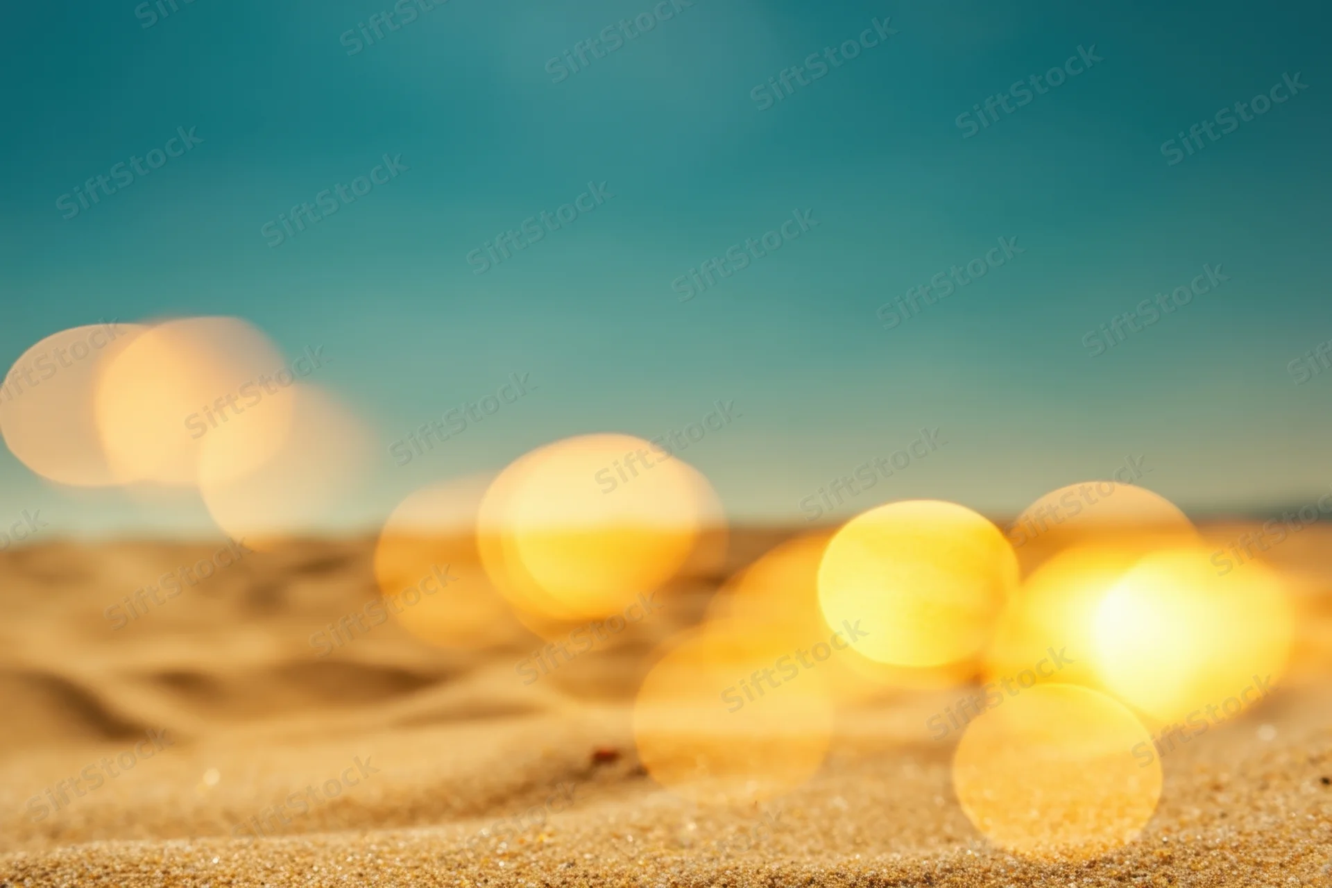 Sunlit golden sand on a beach with blurred lights and blue sky in the background
