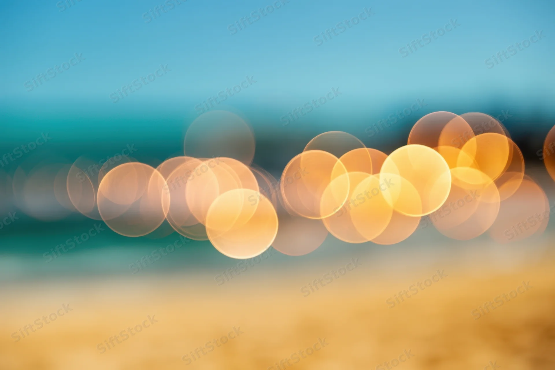 Blurred lights along a sunlit beach with golden sand and blue sky at sunset