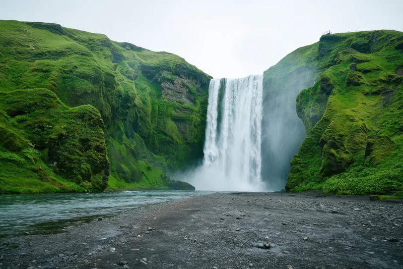 Tall waterfall plunging from moss-covered cliff into river surrounded by green vegetation
