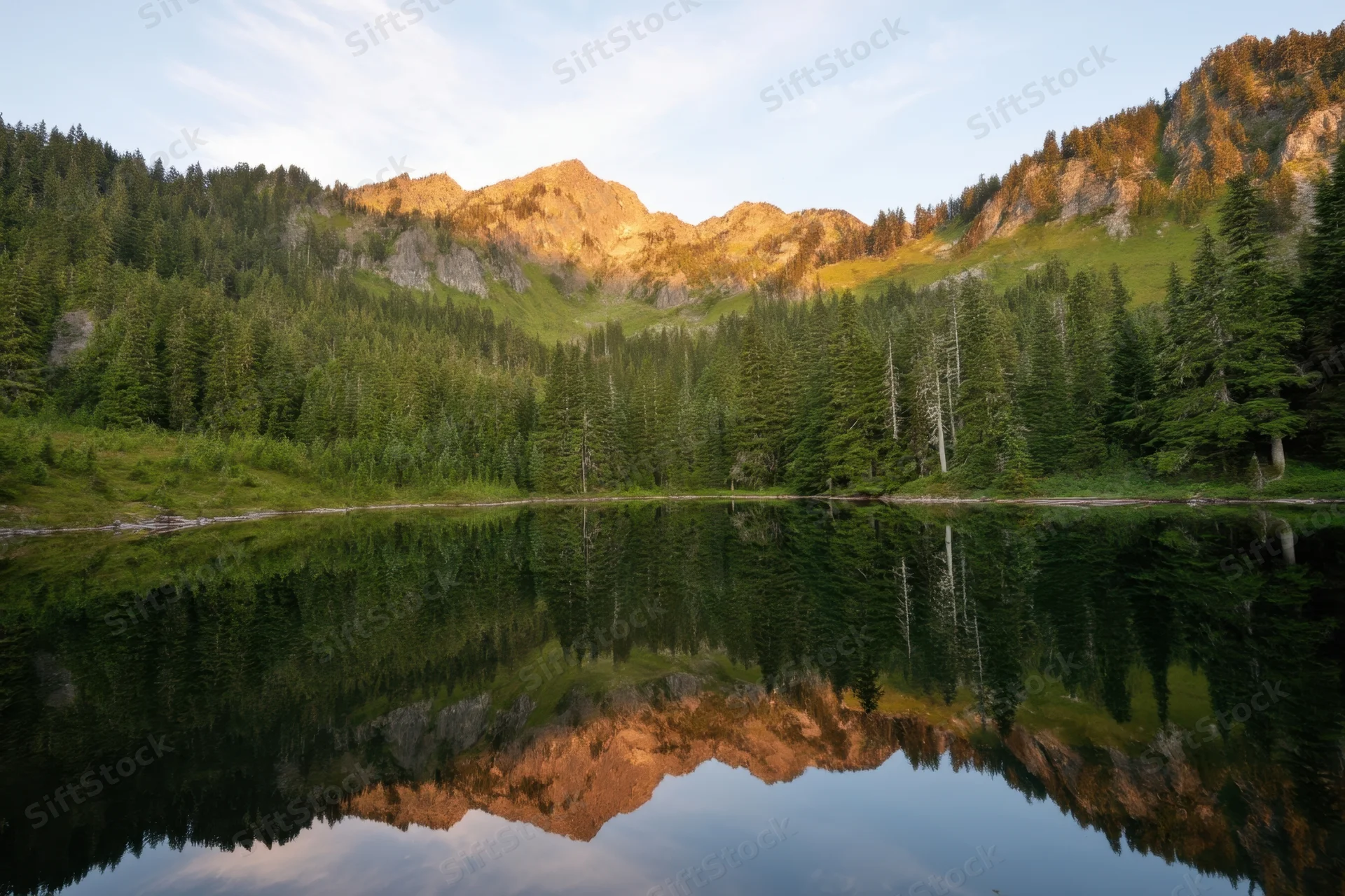 Alpine lake reflecting mountains and evergreen forest at sunrise