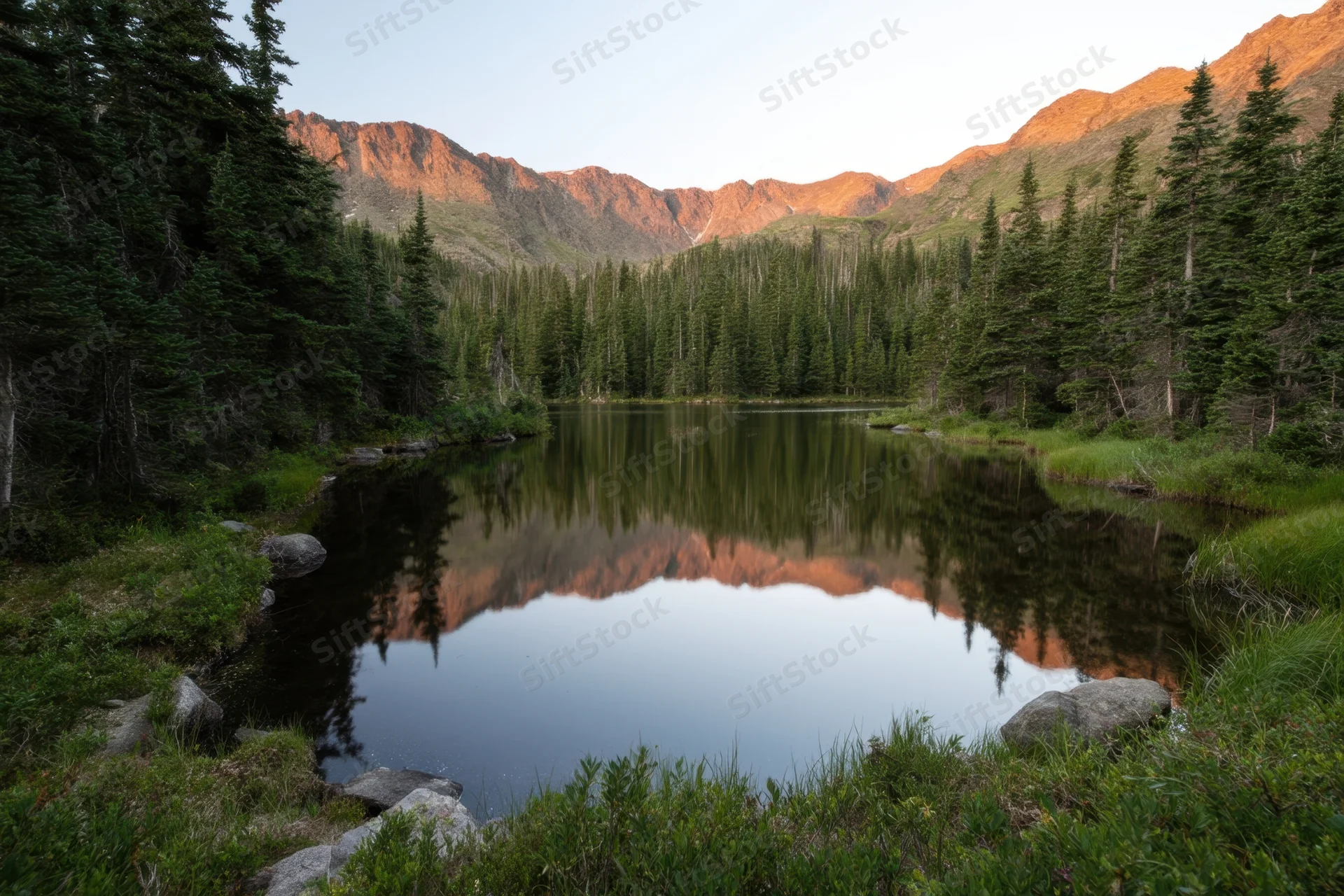 Alpine lake reflecting mountains and evergreen trees surrounded by forest at sunset
