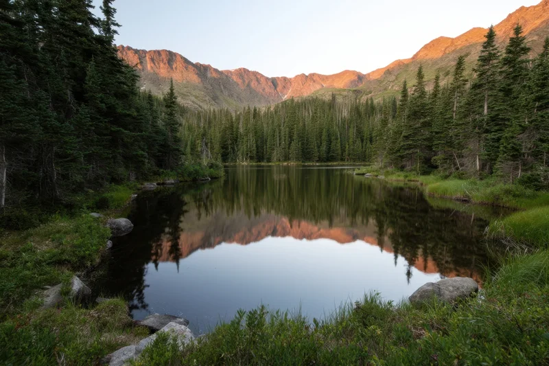Alpine lake reflecting mountains and evergreen trees surrounded by forest at sunset