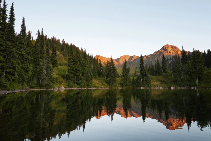 Alpine lake reflecting mountains and evergreen trees at sunset