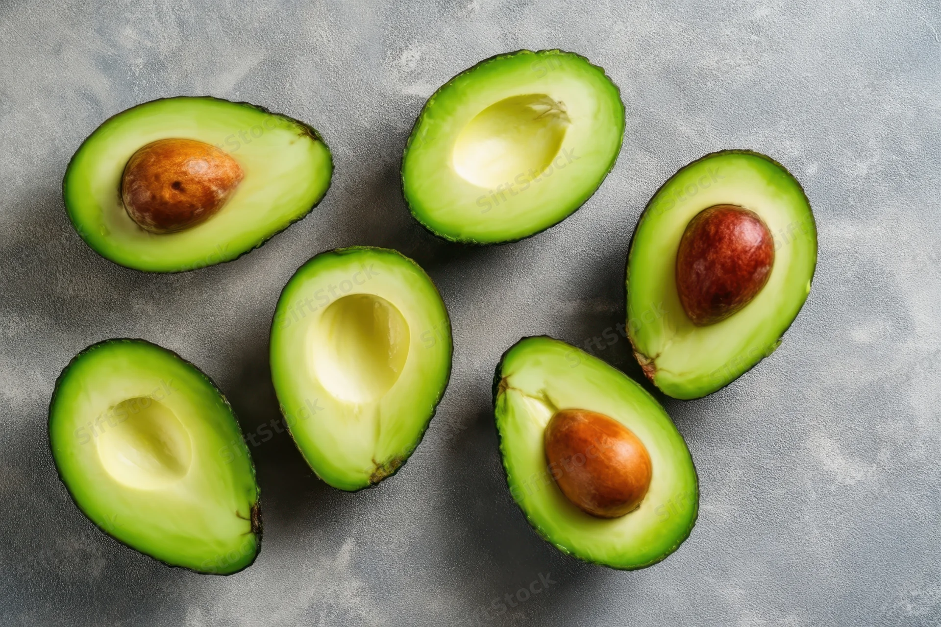 Halved avocados with pits scattered on a gray surface