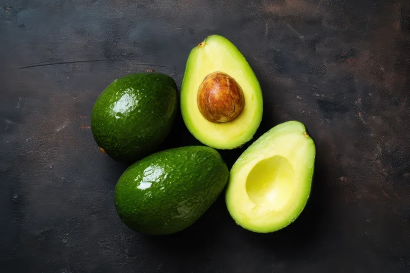 Whole and halved avocados arranged on a dark textured surface