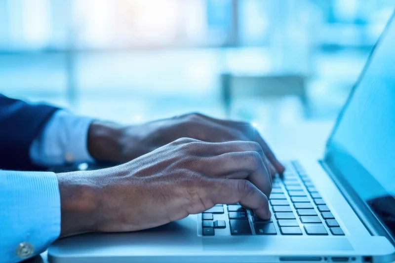 Hands typing on a laptop keyboard in a modern office setting