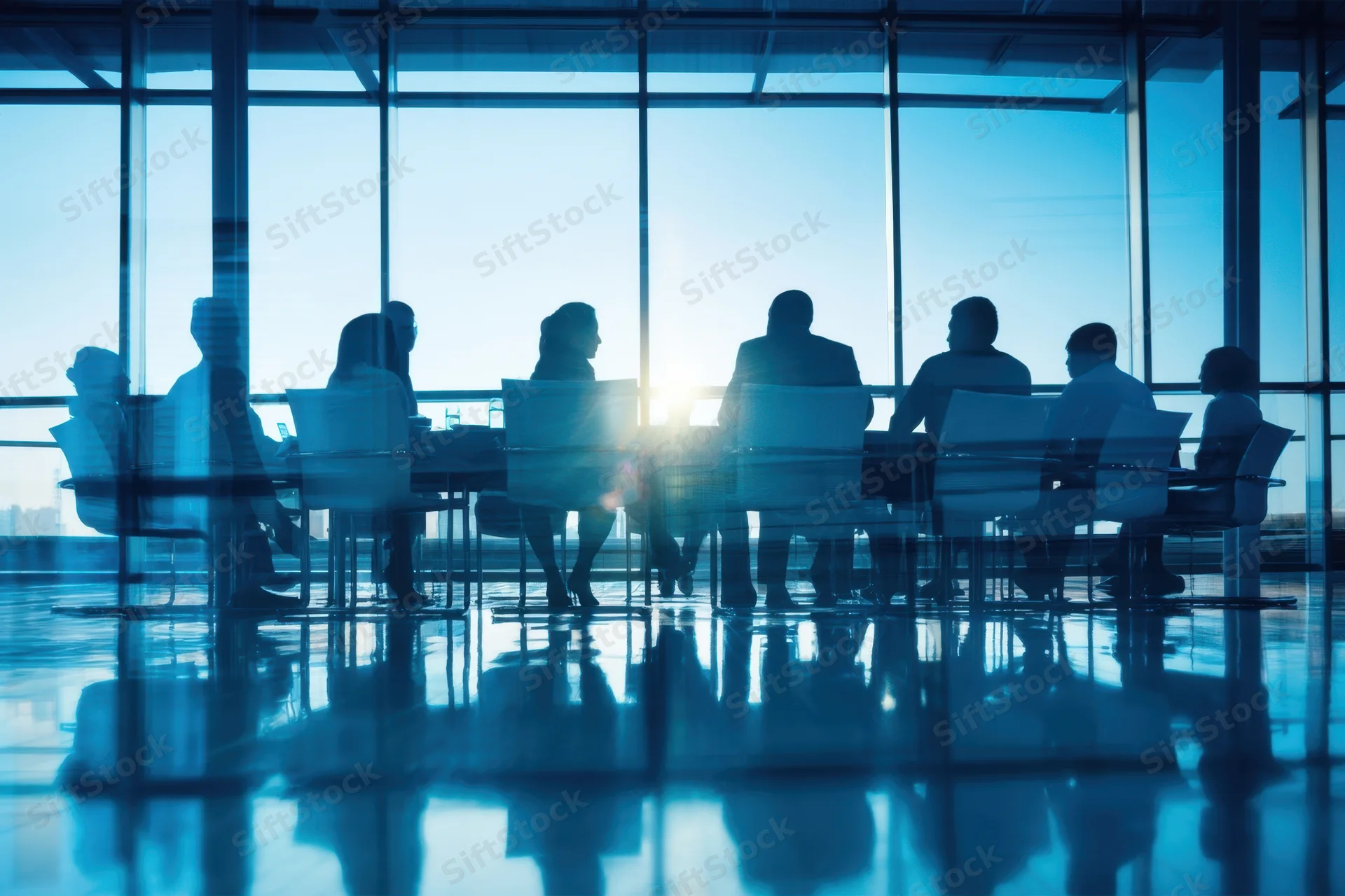 Silhouettes of professionals in a meeting around a glass conference table in a modern office with sunlight through large windows