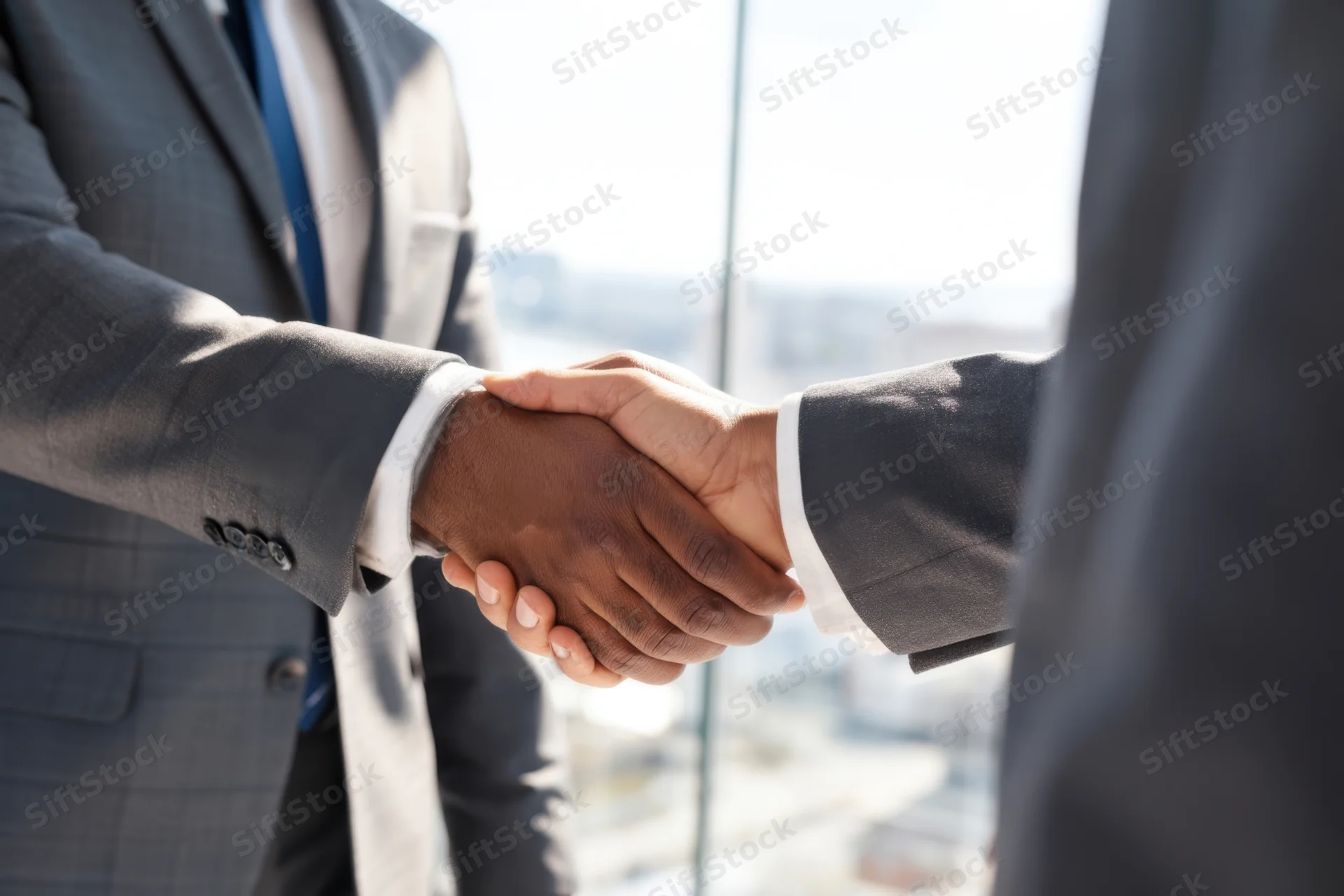Two businessmen in suits shaking hands in a modern glass office with city view