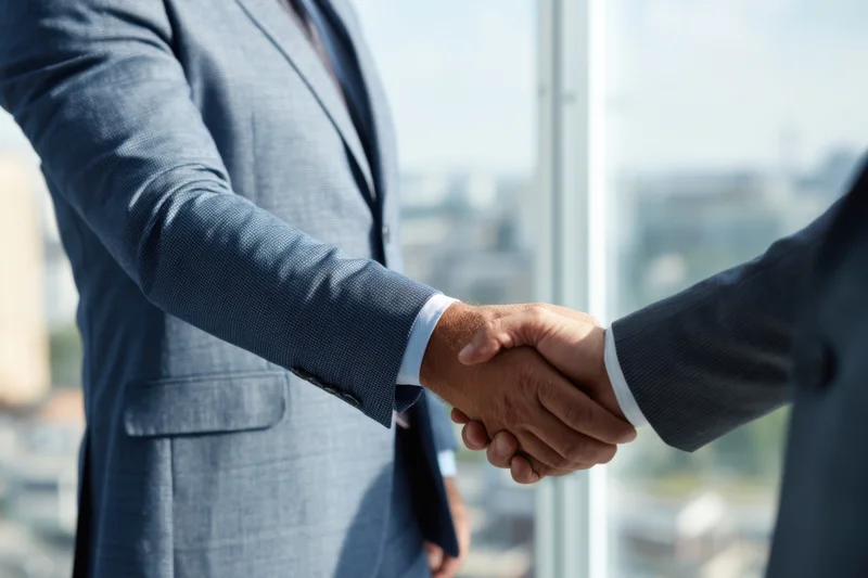 Two men in suits shaking hands in a modern office with city view through glass window