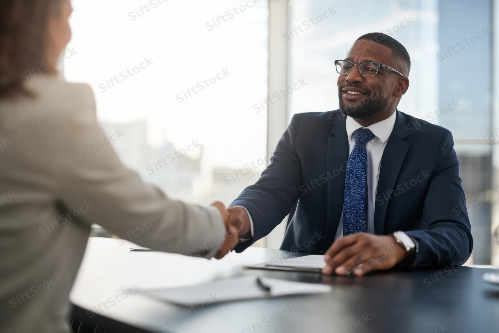 Businessman in suit shaking hands with woman across conference table in office