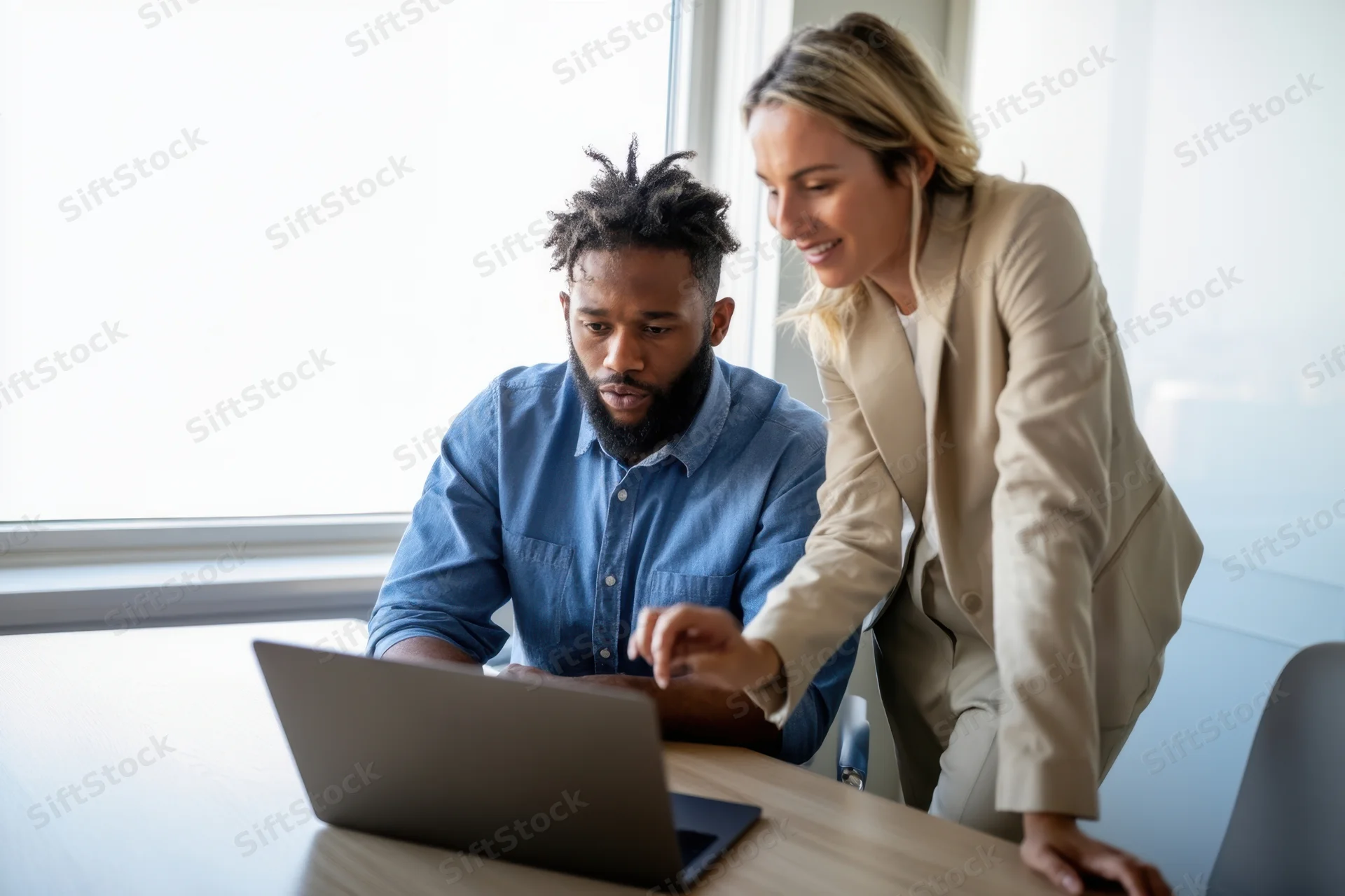 Two colleagues collaborating over a laptop in a bright office