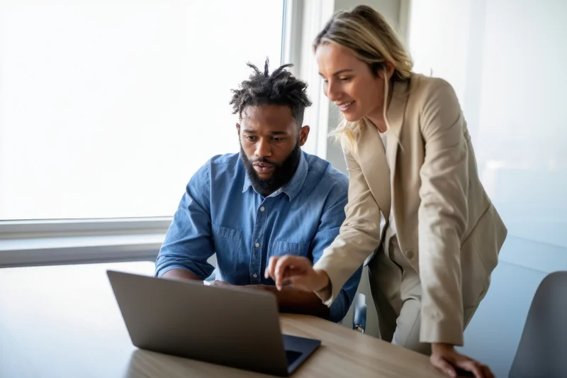 Two colleagues collaborating over a laptop in a bright office