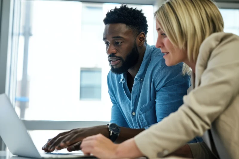 Two colleagues collaborating over a laptop in a bright office