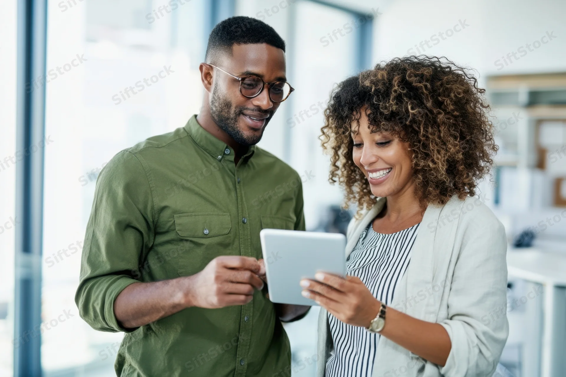 Two coworkers smiling while collaborating on a tablet in a bright modern office