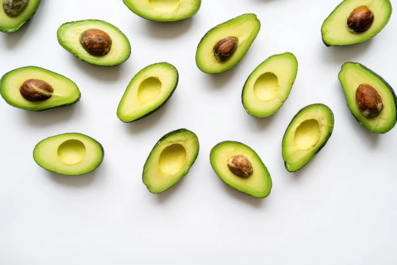 Halved avocados scattered on a white surface with some pits removed