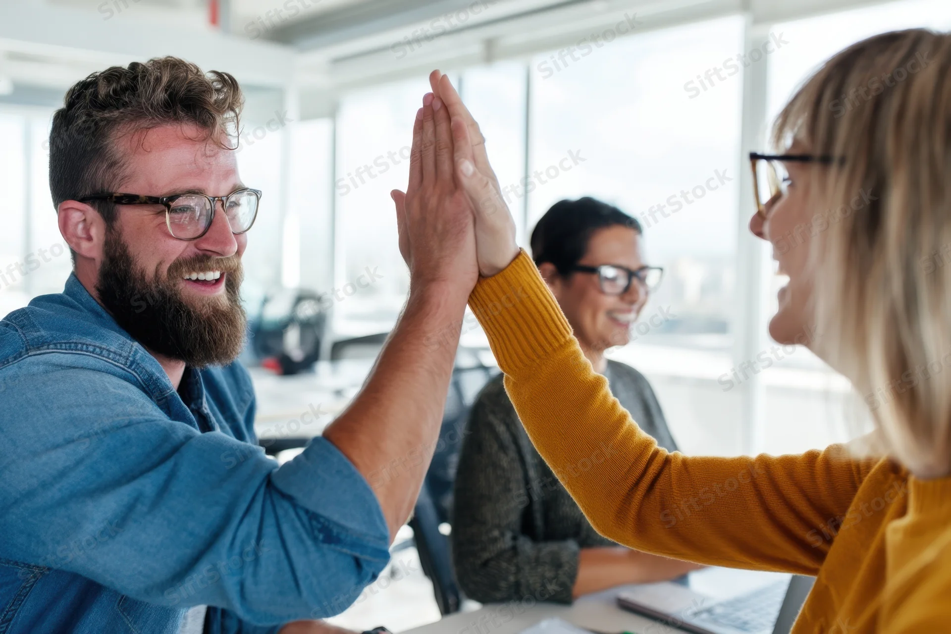 Man and woman high-fiving in office with colleagues in background