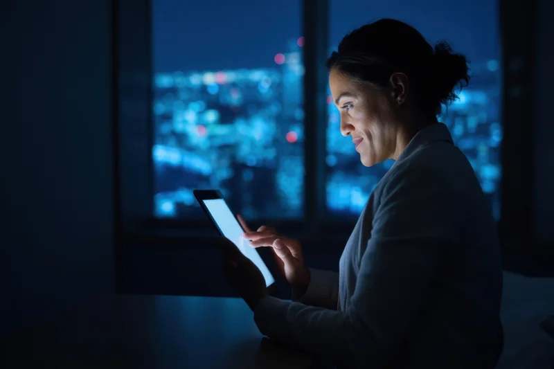 Woman using tablet in dark room with city lights visible through window