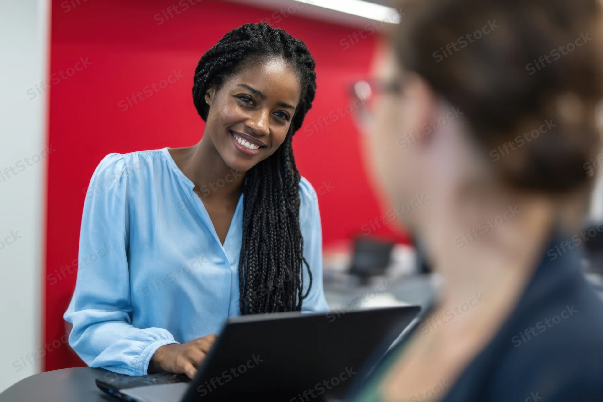 Black woman smiling during office meeting with colleague at desk using laptop