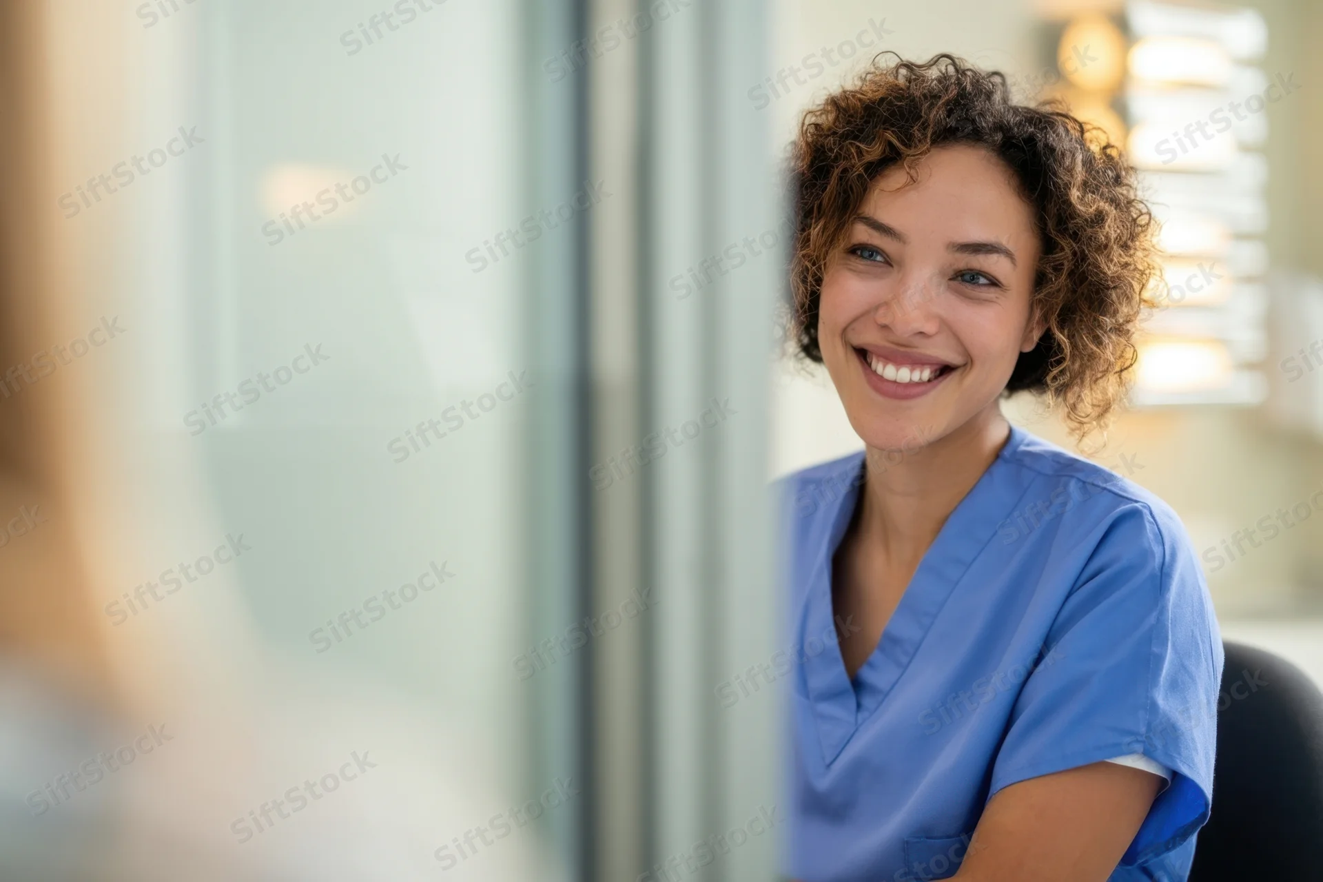 Nurse in blue scrubs smiling during patient consultation in clinic
