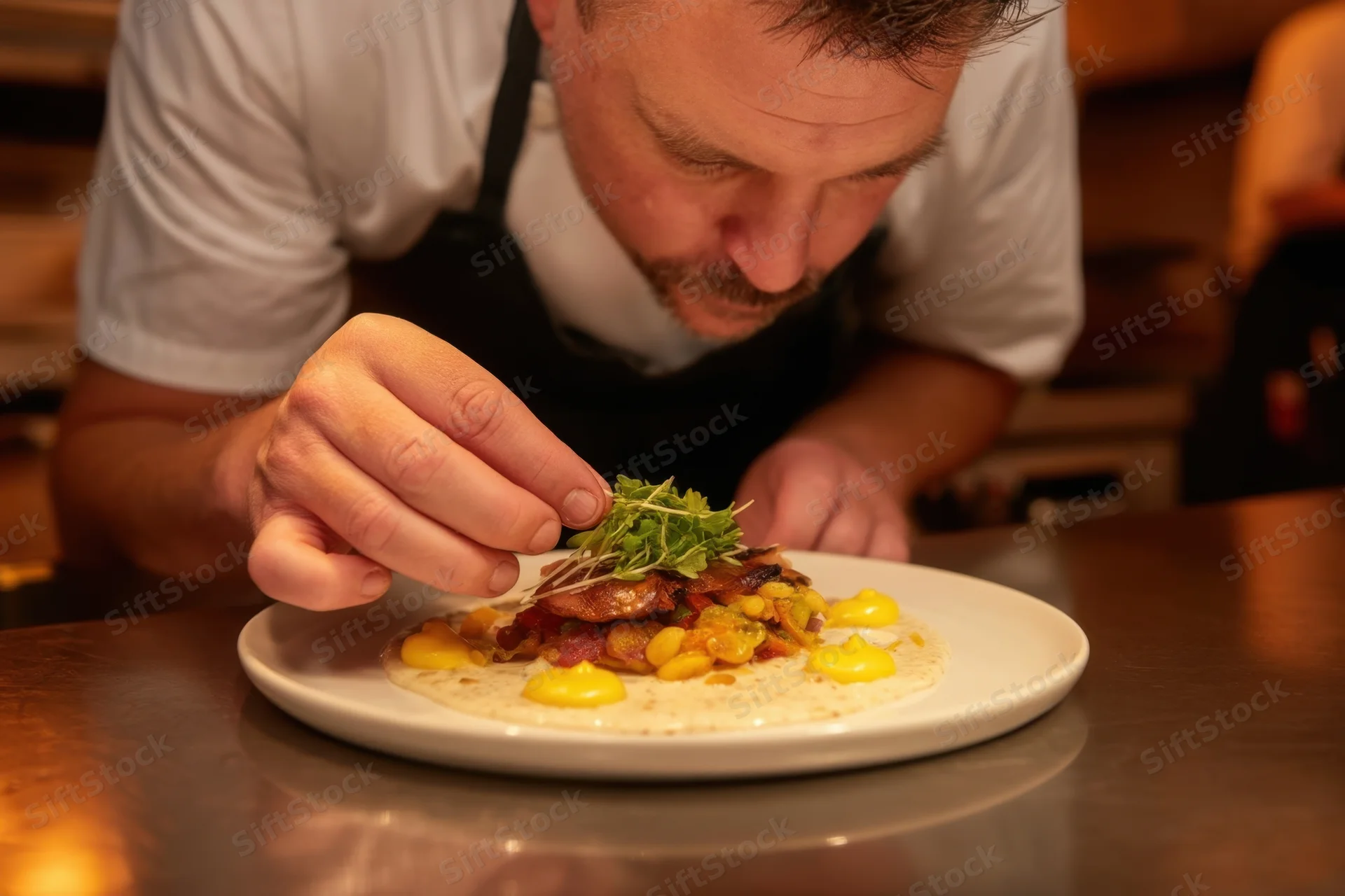 Chef garnishing gourmet dish with microgreens on white plate in kitchen