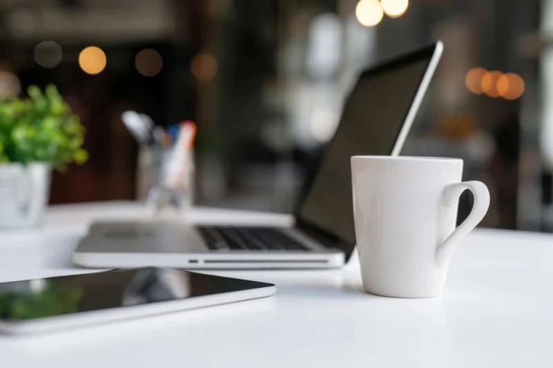 Silver laptop and white mug on a white table in a cafe workspace