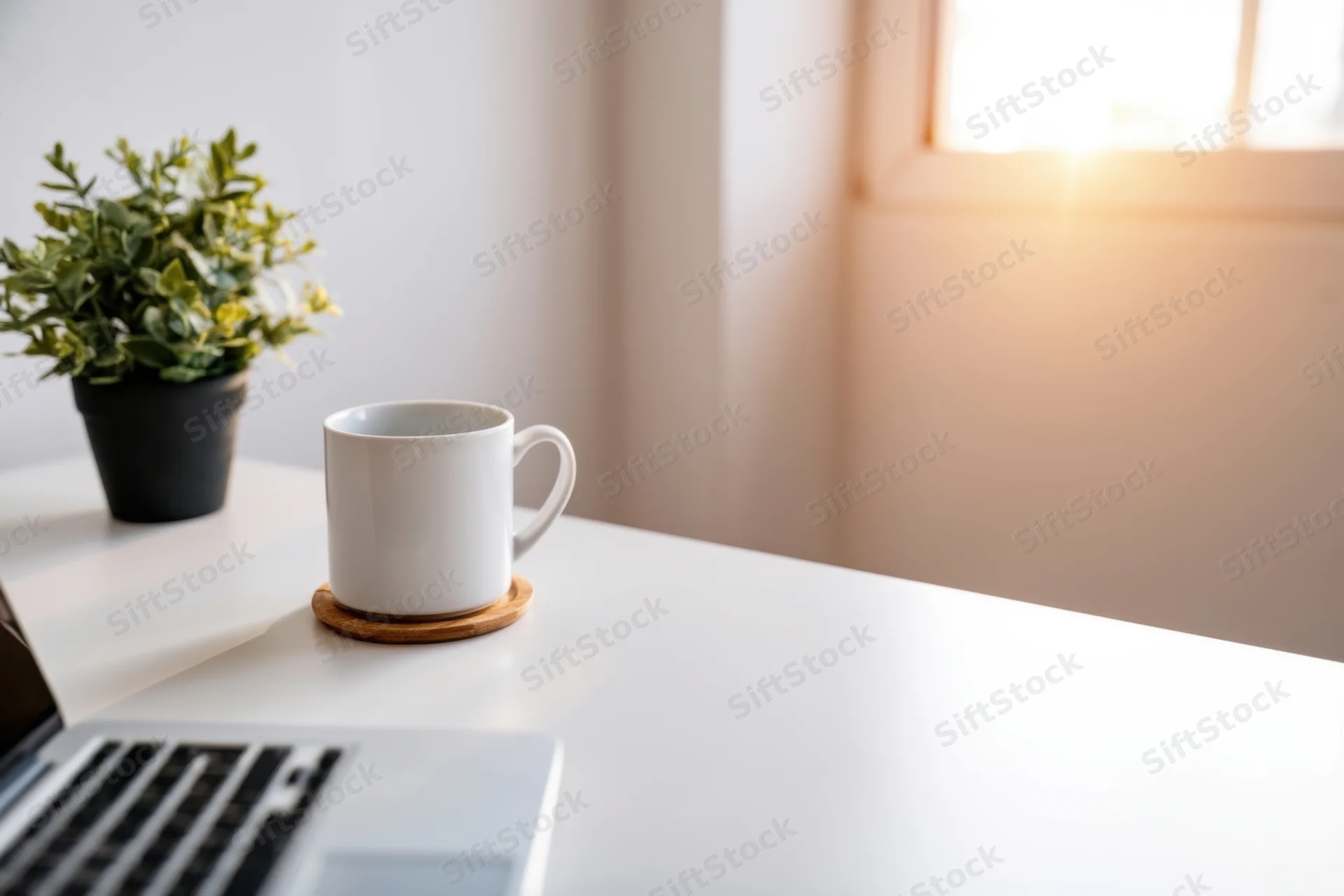 White desk with laptop, mug on coaster, and potted plant near window in home office