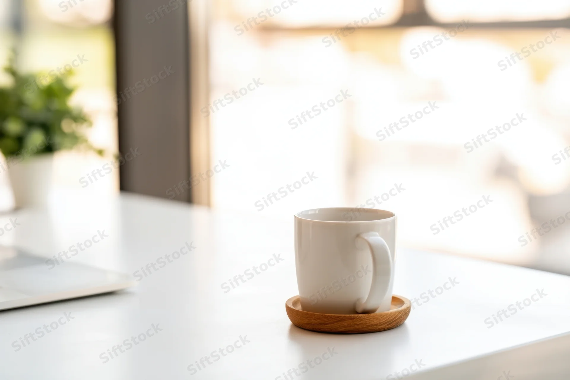 White ceramic mug on wooden coaster on clean desk beside silver laptop near window