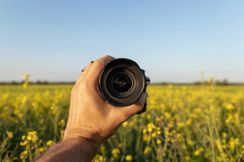Hand holding camera lens over a sunlit canola field in spring