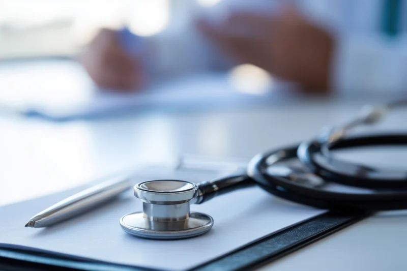 Stethoscope resting on clipboard with pen beside it on desk in clinic setting