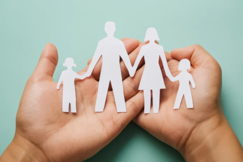 Hands cupping a paper cutout family against a teal background