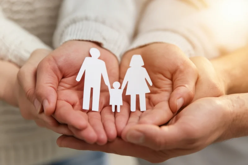 Hands cupping a white paper family cutout in a gesture of care and protection